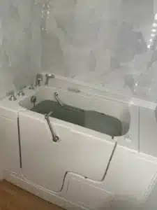 Close-up of a filled white walk-in tub showing the heavy-duty locking handle and marble-patterned wall panels.