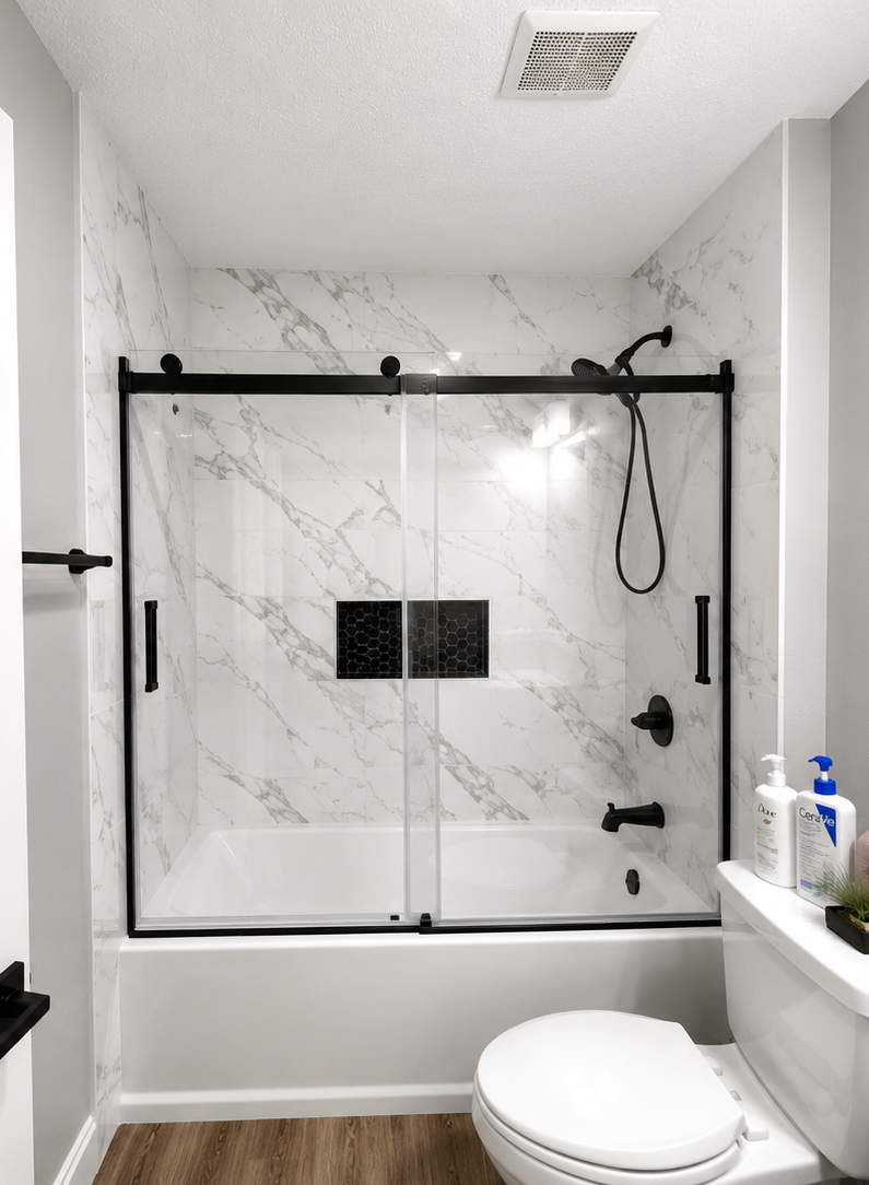 Remodeled Bathroom With Marble-Look Tile Surround, Black-Framed Sliding Glass Shower Door, Bathtub, And Toilet On Wood-Look F