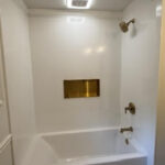 White soaking tub and shower surround with brushed gold fixtures and built-in niche shelf, tub renovation in Delaware, Ohio